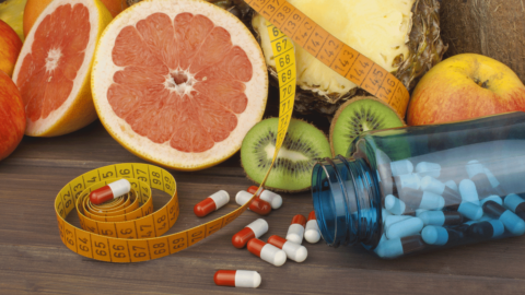 Weight loss pills spilled from a bottle next to fresh fruits and a measuring tape, symbolizing the evolution of weight loss methods from diet supplements to modern medication