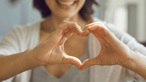 Smiling woman forming a heart shape with her hands to symbolize heart health and wellness from GLP-1 weight loss medications