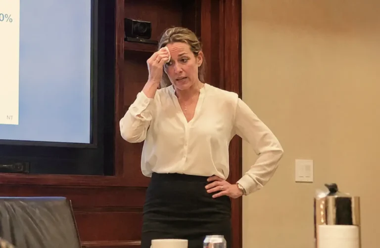 A woman dabs sweat from her forehead while presenting in a professional setting, visibly experiencing anxiety symptoms that a QuickMD provider can help diagnose and treat.
