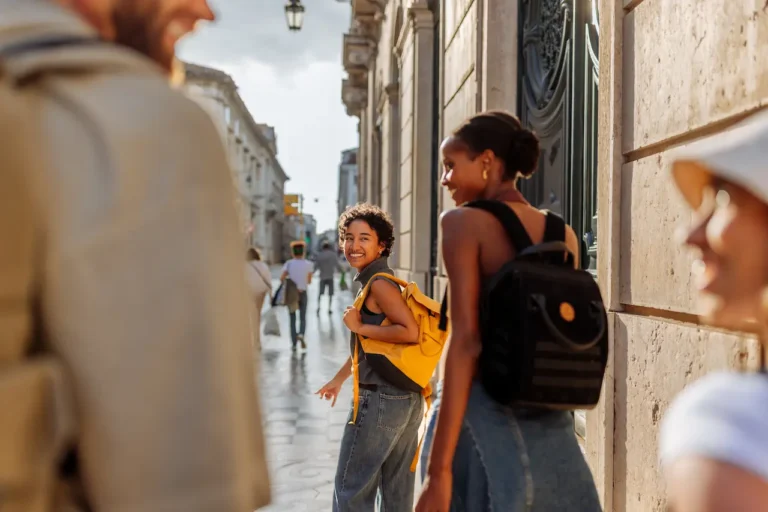 Two smiling women with backpacks walking together on a sunny city street, representing hope and recovery from opioid addiction
