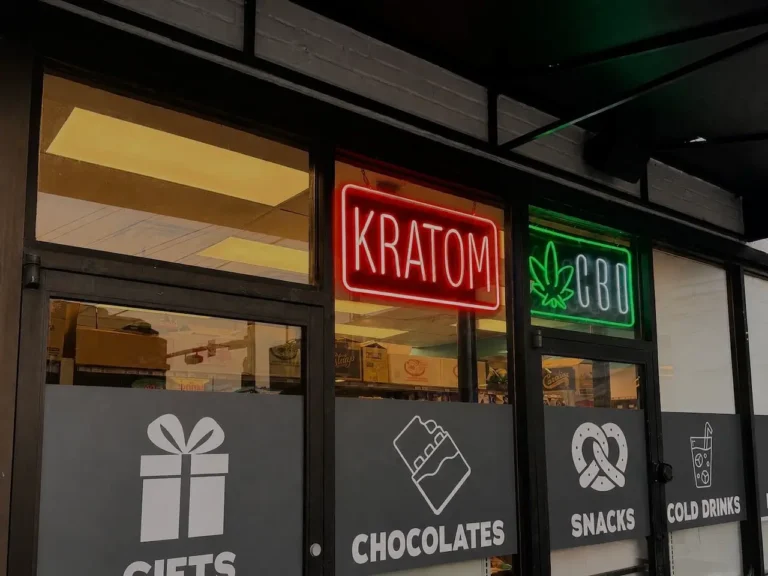 storefront-window-displaying-red-neon-kratom-and-green-neon-CBD-signs-with-decals-for-gifts-chocolates-snacks-and-cold-drinks