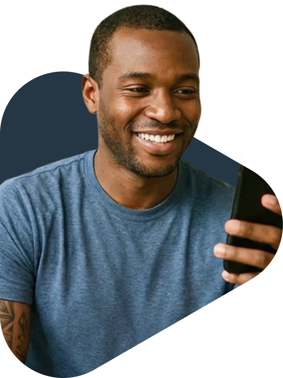 Smiling young man in a blue t-shirt holding a smartphone, looking at the screen with a tattooed arm visible