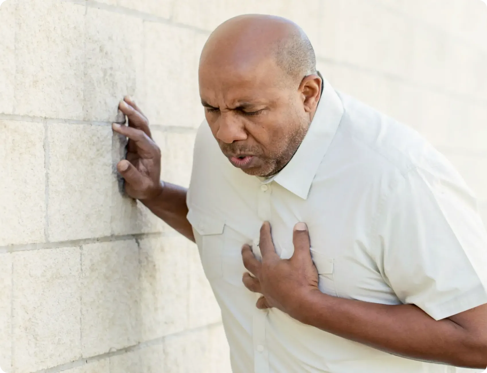 Middle-aged man clutching his chest in pain while leaning against a wall, showing signs of a heart attack