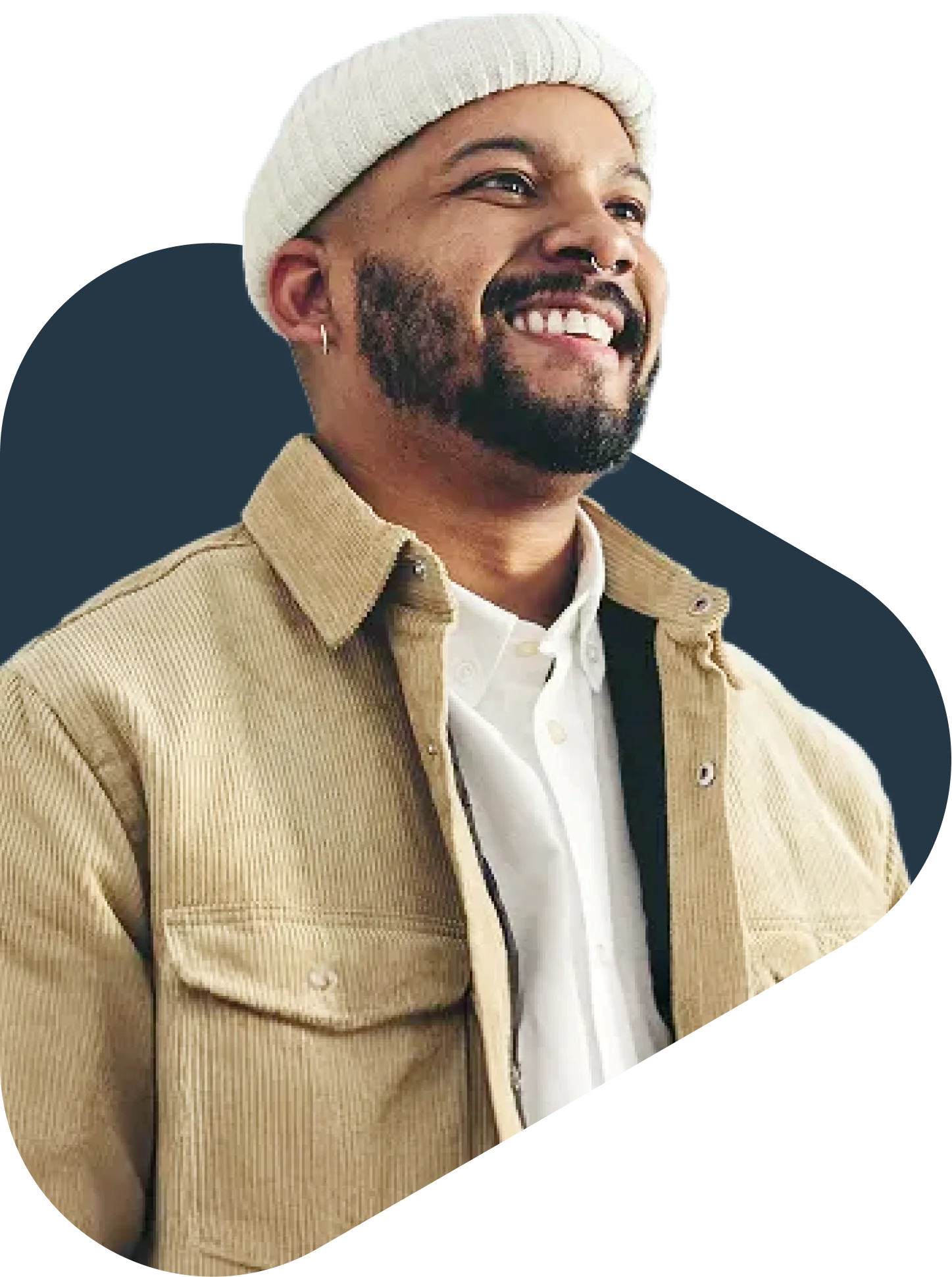 Smiling man with a white beanie, beard, and tan corduroy jacket over a white shirt, looking upward cheerfully.