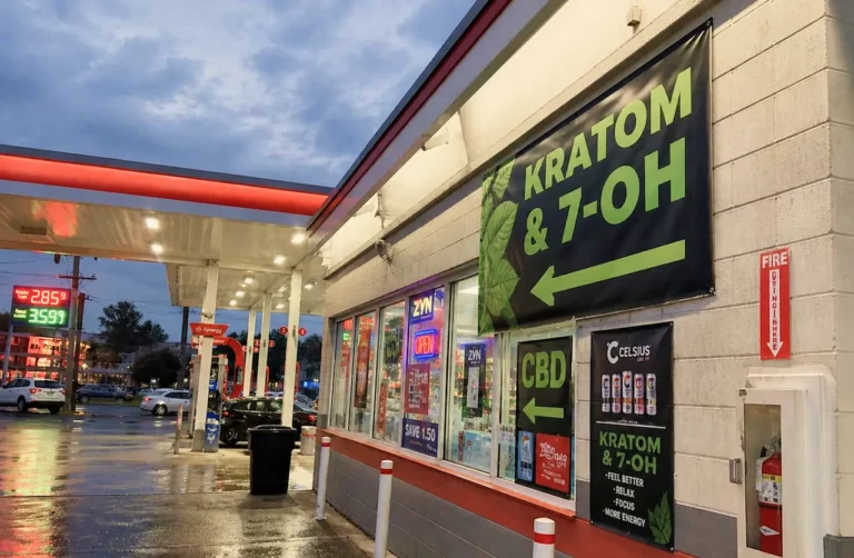 Gas station convenience store displaying large signs advertising kratom, 7-OH, and CBD products for sale at dusk.