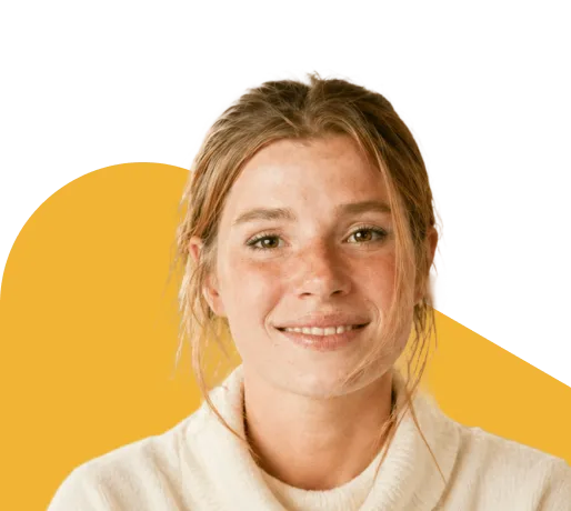 Young woman with freckles smiling confidently, wearing a cream sweater against a warm yellow background, representing mental health wellness.