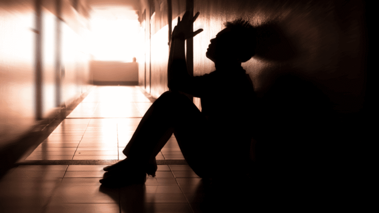 Silhouette of a person sitting against a wall in a dimly lit hallway, symbolizing the effects of Suboxone, its role in opioid addiction treatment, and the reality of buprenorphine&rsquo;s impact on euphoria