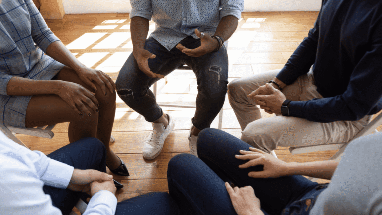 Group therapy session with people sitting in a circle, discussing opioid addiction treatment options, including at-home recovery alternatives