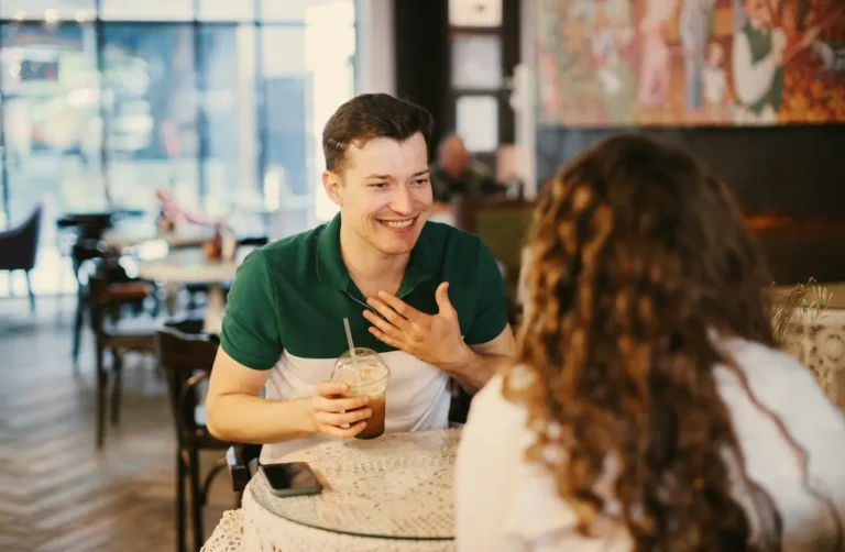 Man smiling and talking with a woman over coffee at a caf&eacute;, representing social connection and dating during recovery from opioid use disorder with support from telehealth care like QuickMD.