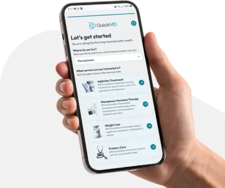Hand holding a smartphone displaying the QuickMD app onboarding screen with telehealth service options including addiction treatment and weight loss.