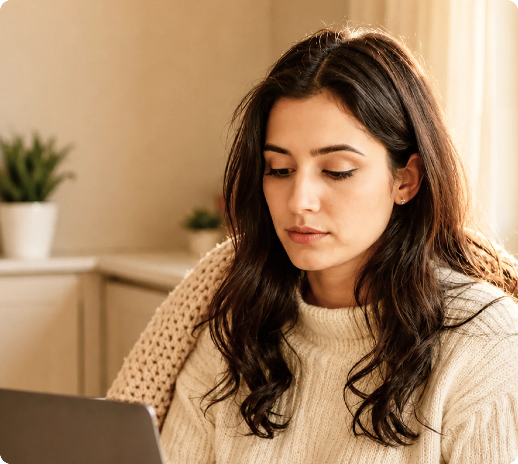 Young woman in a cream sweater using a laptop at home, seeking online urgent care services