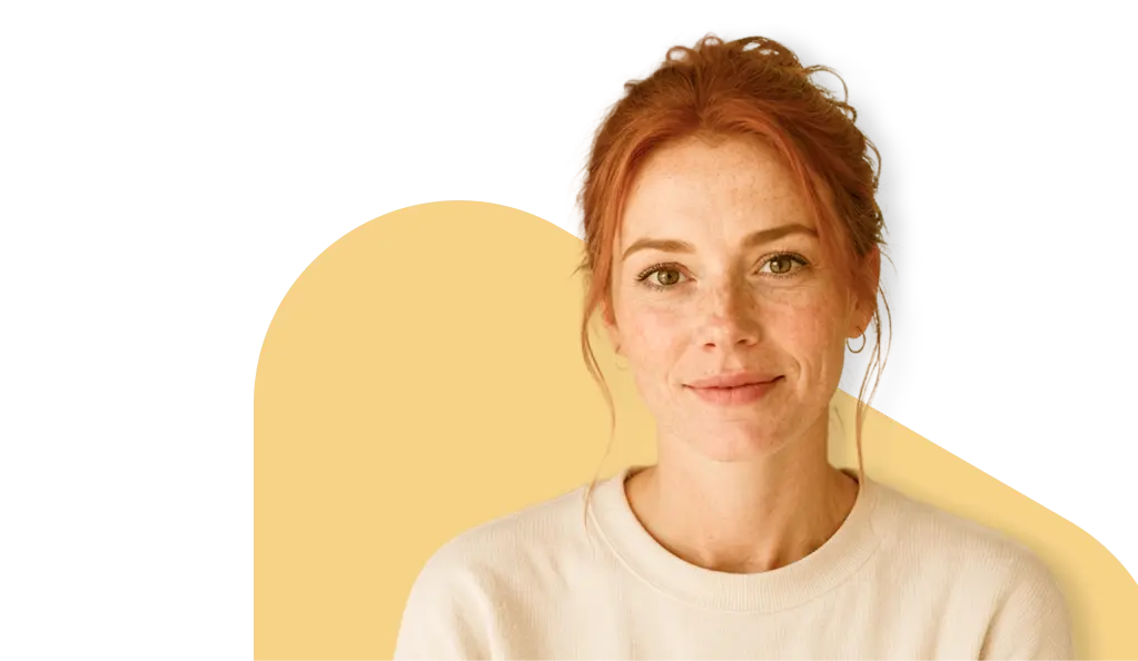 Young woman with red hair and freckles smiling softly, wearing a white sweater, seeking urgent care telehealth services