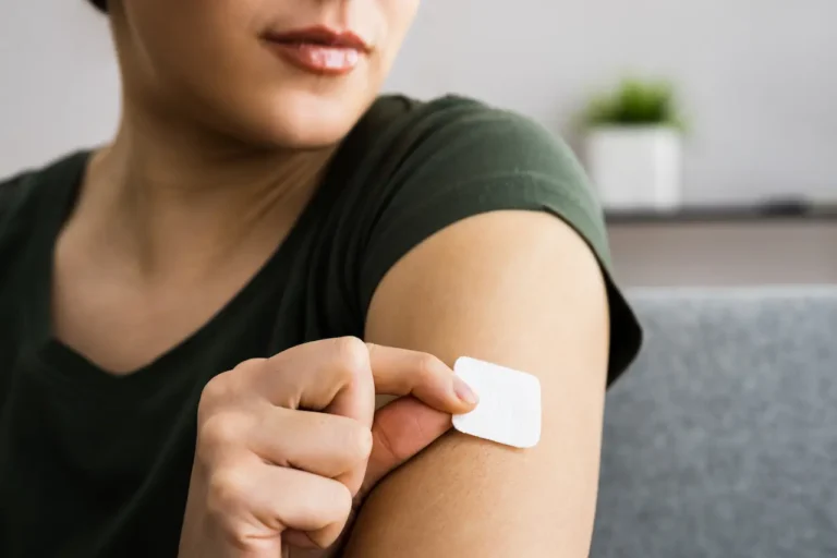 Woman applying a transdermal estrogen hormone therapy patch to her upper arm during menopause treatment shortage