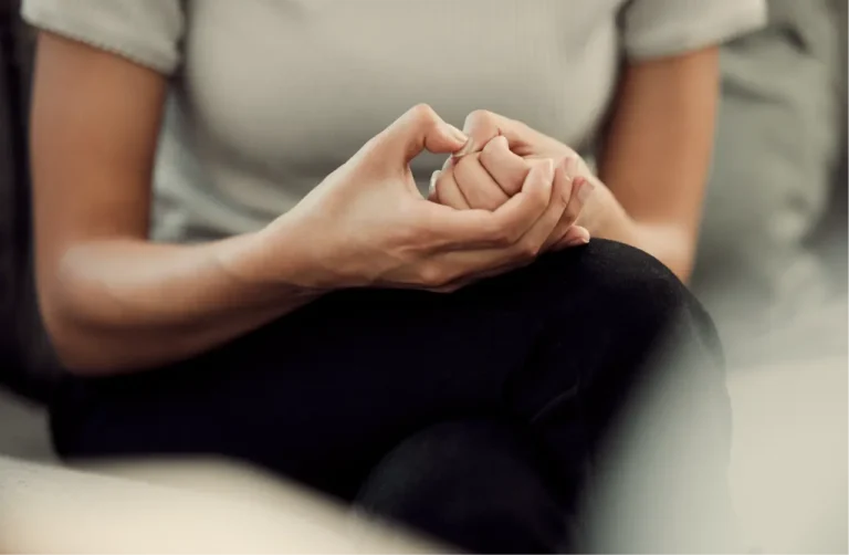 Person nervously wringing hands together on lap, showing common physical anxiety symptoms and stress body language