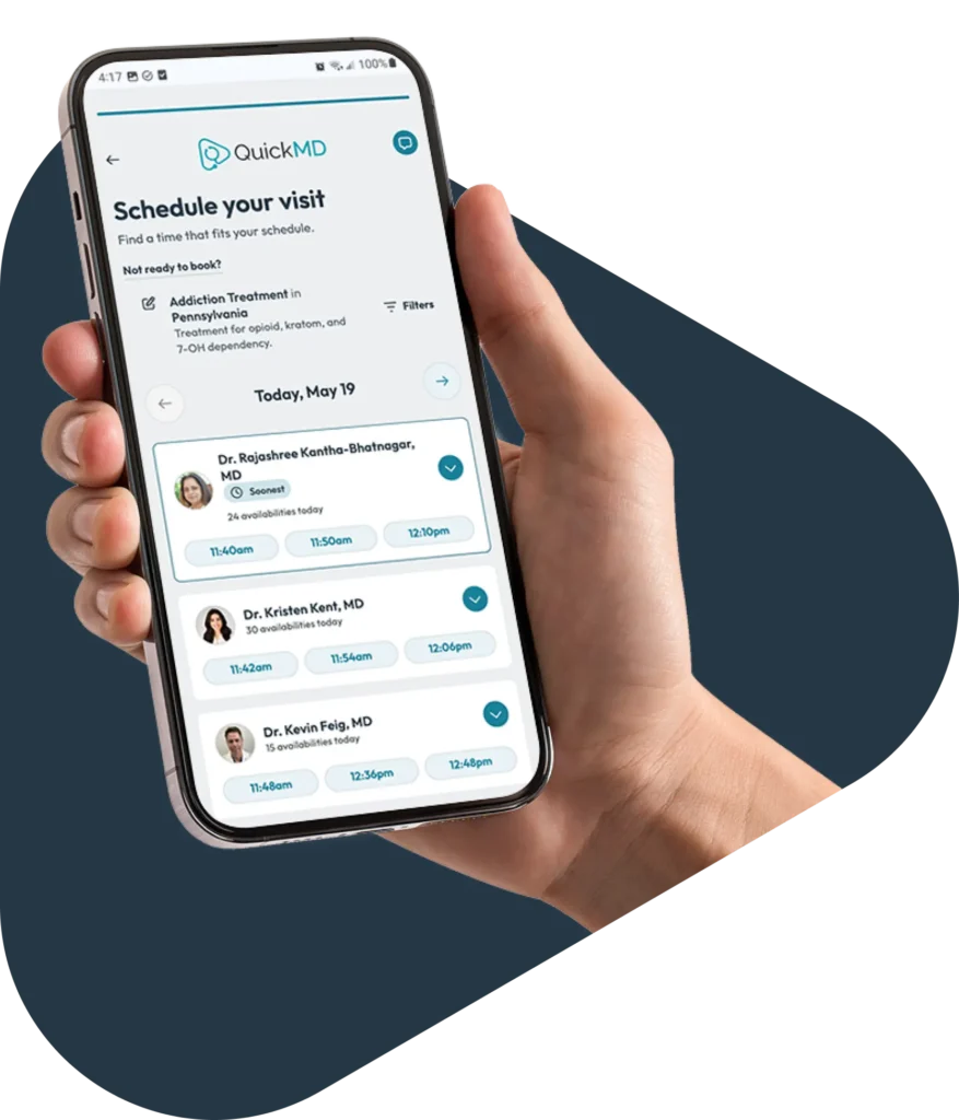 Hand holding a smartphone displaying the QuickMD app's clinician scheduling screen with available appointment times
