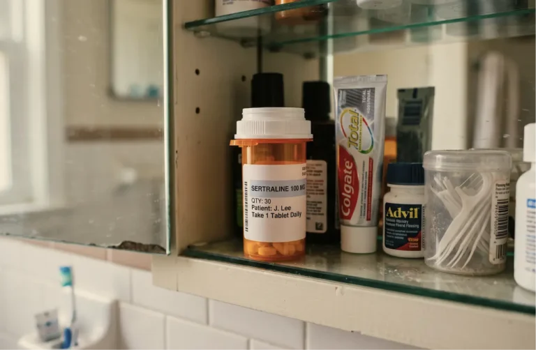 Sertraline 100mg prescription bottle in a bathroom medicine cabinet alongside Colgate toothpaste, Advil, and cotton swabs
