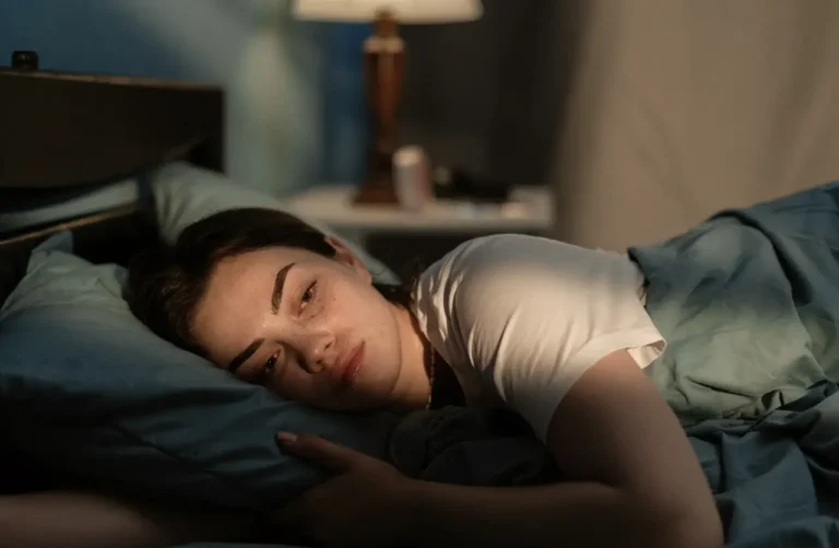 Young woman lying awake in bed at night with a worried expression, struggling with anxiety and sleeplessness