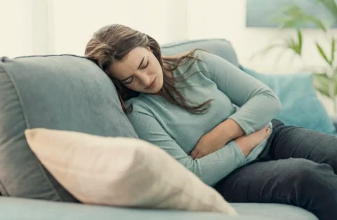 Woman lying on a couch holding her abdomen in pain, illustrating potential gallbladder issues or side effects associated with medications like Ozempic.