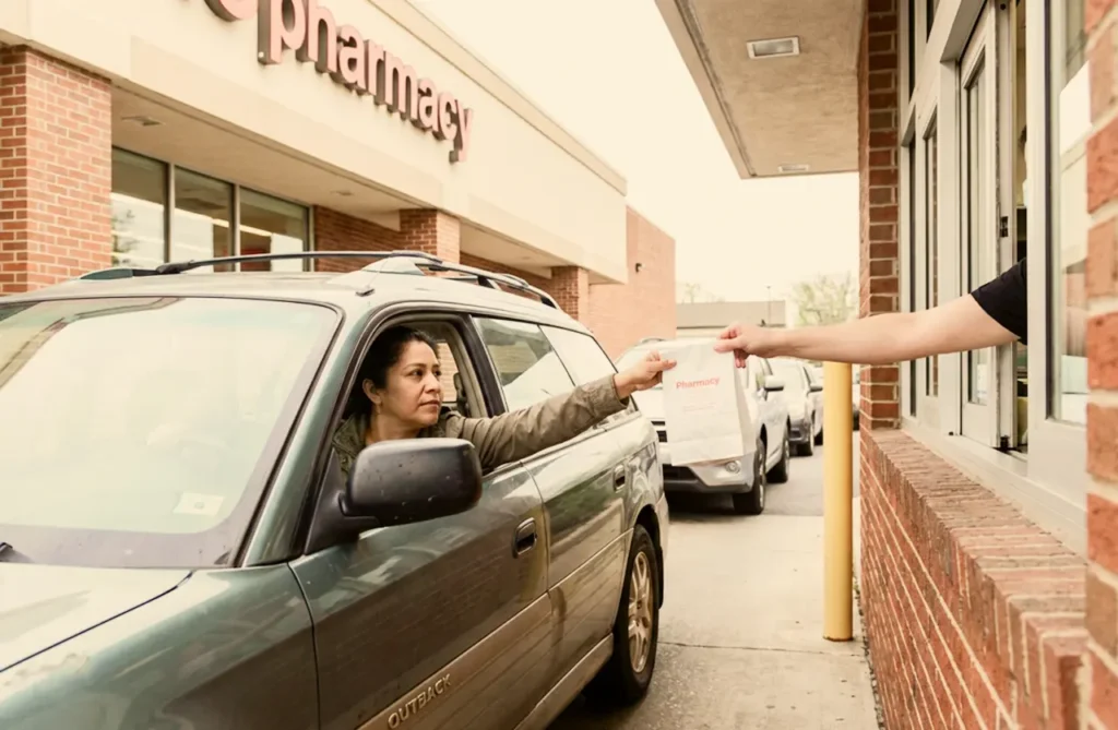 A woman picks up a prescription bag at a pharmacy drive-through window, illustrating the cost of Rybelsus with and without insurance