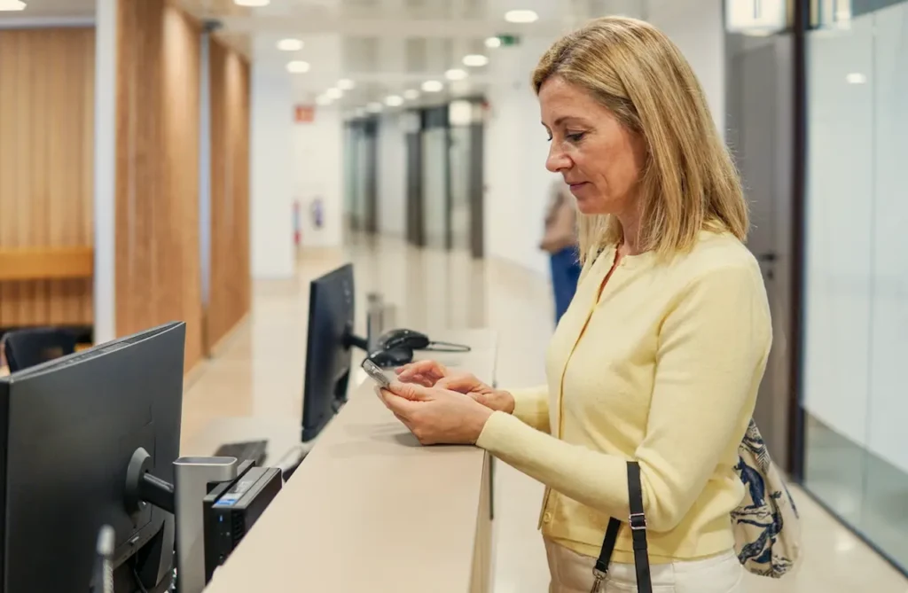 Middle-aged woman checking in at a medical office reception desk, representing routine screenings like Pap smears after menopause.