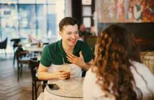Man smiling and talking with a woman over coffee at a café, representing social connection and dating during recovery from opioid use disorder with support from telehealth care like QuickMD.