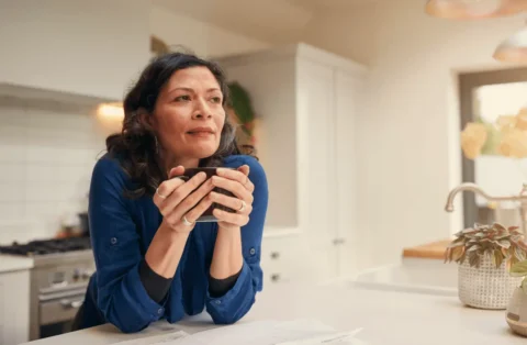 woman-holding-coffee-mug-in-kitchen-thinking